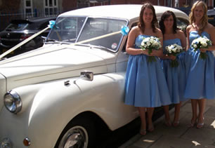 Bridesmaids hold flowers and stand next to wedding car